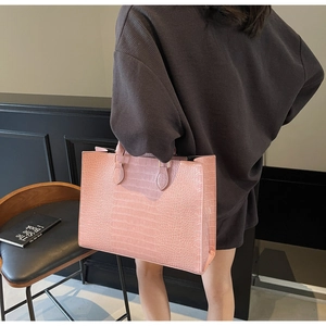 Pink crocodile pattern tote bag shown held by a model in a high-fashion editorial setting