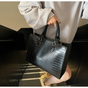 Detail of black crocodile pattern tote bag featuring gold hardware in a street style setting