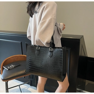 Detail of black crocodile texture large tote bag held by a model in modern interior