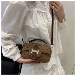 Détail d'un sac bandoulière vintage marron imprimé avec fermoir doré sur chemise dentelle