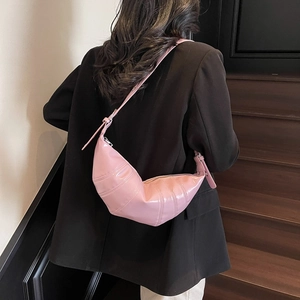 Pink croissant bag with pleated details worn by a model in a minimalist urban setting