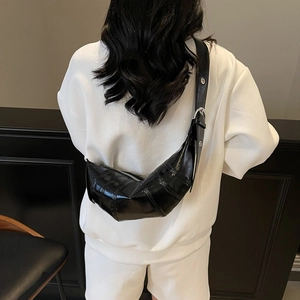 Black glossy croissant shoulder bag with adjustable eyelet strap on a model