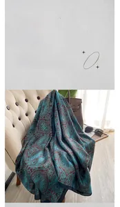Detail of silk satin scarf with teal paisley pattern draped on a chair with accessories