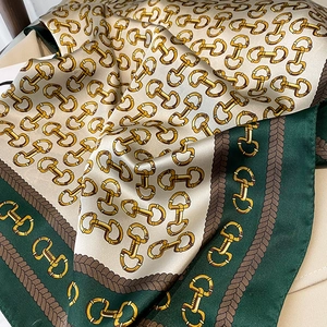 Close-up of silk square scarf showing gold horsebit pattern and green hem texture