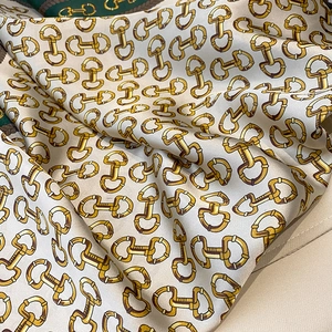 Macro view of silk-like champagne square scarf with classic gold snaffle bit pattern