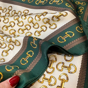 Macro detail showing smooth satin texture and equestrian horsebit pattern of the scarf
