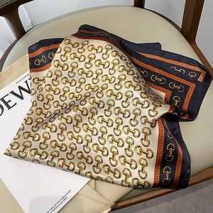 Close-up of silk scarf with gold chain and horsebit print on cream background