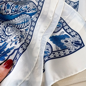 Detailed macro view of white silk-like scarf featuring blue paisley and floral patterns