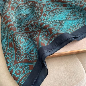 Teal and brown paisley silk scarf with satin edges displayed on a soft velvet surface