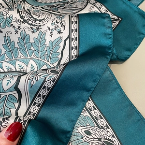 Detailed macro view of paisley pattern and satin texture on a teal floral silk scarf