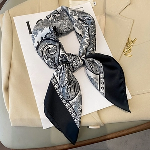 Elegant paisley floral square silk scarf with black border laid on a beige suit jacket