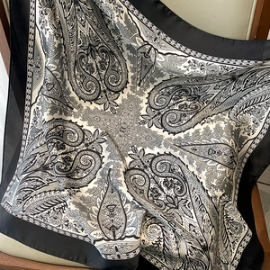 Detail of elegant black and white paisley silk scarf draped over a chair, satin texture