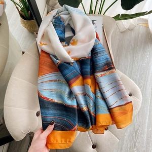 Silk-feel scarf with wave pattern and bird print folded elegantly on a soft chair