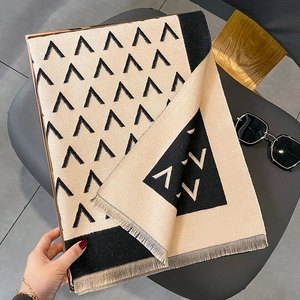 Winter beige and black knit scarf with geometric V-pattern and grey tassels on leather seat