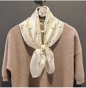 Detail of cream silk scarf with black bird print draped on a brown knit sweater