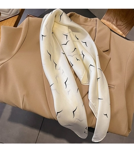Detail of elegant cream silk scarf with black bird pattern styled on a camel blazer