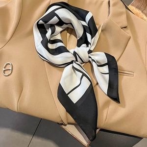 Elegant black and white geometric silk scarf tied in a bow on a beige blazer jacket
