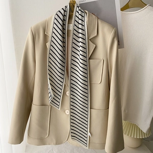 Detail of a black and white striped skinny scarf paired with a beige blazer for a French look