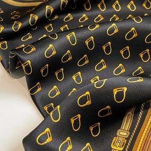 Macro view of black silk scarf with golden stirrup print and satin finish texture