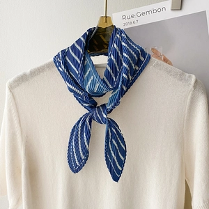 Blue and white striped pleated skinny scarf tied on a white sweater with a golden hanger