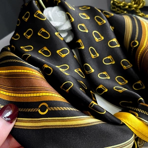 Detail of silk scarf with golden horse bit chains and harness patterns on black fabric