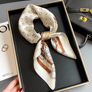 Elegant silk scarf with horse-bit pattern on a minimalist black tray for styling