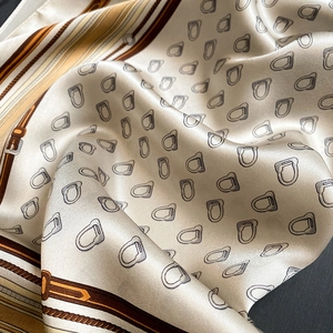 Close-up of champagne silk scarf with equestrian stirrup patterns and satin texture