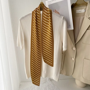 Detail of a pleated yellow striped skinny scarf styled on a white shirt with a cozy backdrop