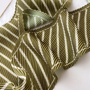 Close-up of pleated silk scarf showing elegant dark green and white diagonal stripes texture