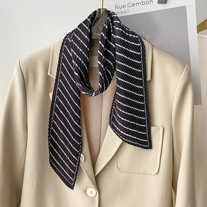Detail of black and white striped pleated silk scarf paired with a beige blazer jacket