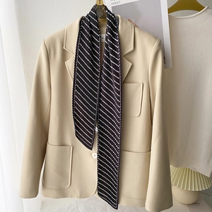 Detail of a beige blazer paired with a black and white striped pleated skinny scarf