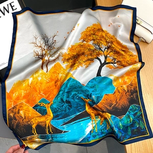Foulard en soie avec motif cerf doré et montagnes exposé avec un sac à main blanc
