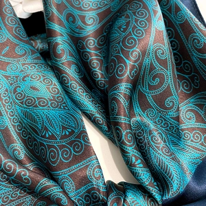 Close-up of luxury silk scarf showing intricate green paisley pattern on dark brown satin fabric