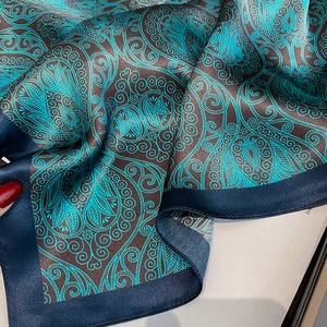 Detail of silk scarf showing paisley pattern in teal and brown with satin edges