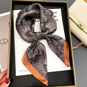 Brown silk scarf with white Paisley pattern and orange border presented on a magazine