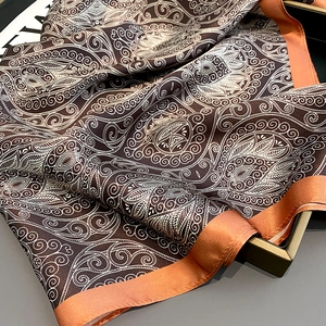 Macro view of paisley silk scarf featuring rich coffee brown and caramel orange satin edges