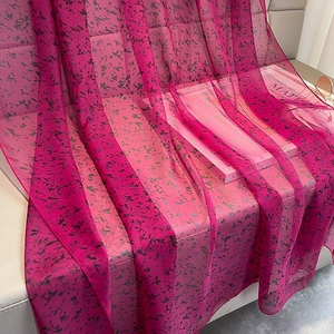 Détail de la texture d'une écharpe en soie rose fleurie drapée sur un canapé blanc