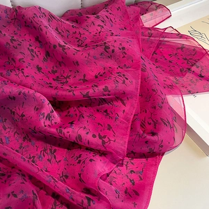 Détail d'une écharpe légère en mousseline rose avec motif de feuilles sombres délicates