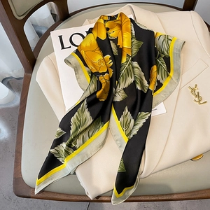 Detail of silk square scarf with yellow roses on black fabric draped over a beige blazer