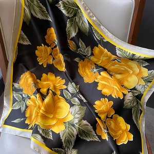 Elegant silk scarf with yellow rose print on black background draped over a chair