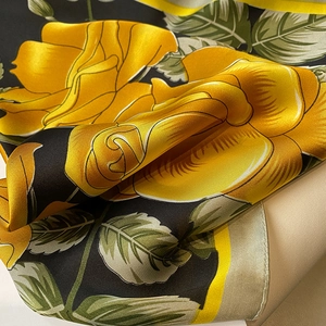 Macro detail of silk scarf featuring yellow roses and green leaves on black background