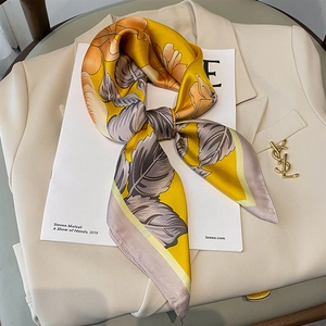 Elegant floral silk square scarf in ginger yellow displayed on a stylish beige blazer