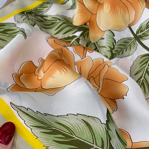 Close-up of silk-textured square scarf featuring orange rose floral prints and elegant drape