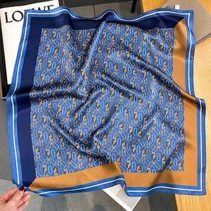 Silk square scarf with blue and gold chain print displayed on a wooden surface