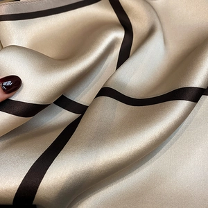 Macro shot of silk plaid scarf texture showing glossy champagne gold fabric and black grid