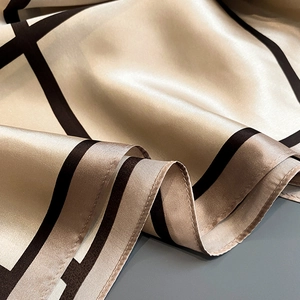 Macro shot of champagne gold silk scarf showing smooth satin texture and black plaid pattern