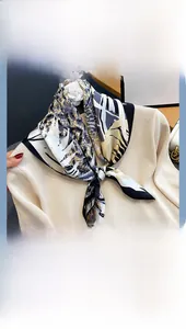 Detail of silk square scarf with blue and gold floral patterns on a beige knit top