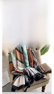 Detail of silk satin scarf with mint green and orange blocks draped over a beige chair