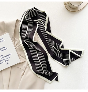 Dettaglio di un foulard twilly in raso a righe bianche e nere su un blazer beige