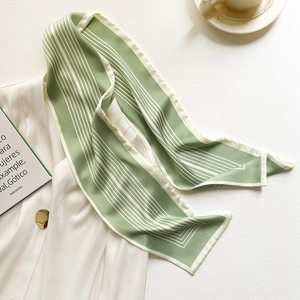 Dettaglio di sciarpa in seta a righe verde salvia su blazer bianco con bottone d'oro